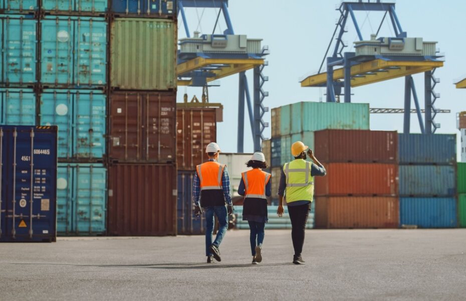 Workers walking through a shipping cargo container terminal depot.