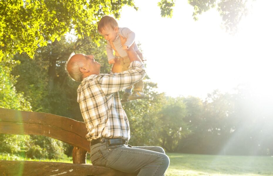A grandfather playing with his young grandson in a park.