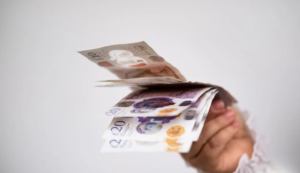 A hand holding UK bank notes.